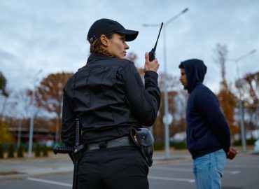 View from back on woman cop in uniform using portable radio for police communication